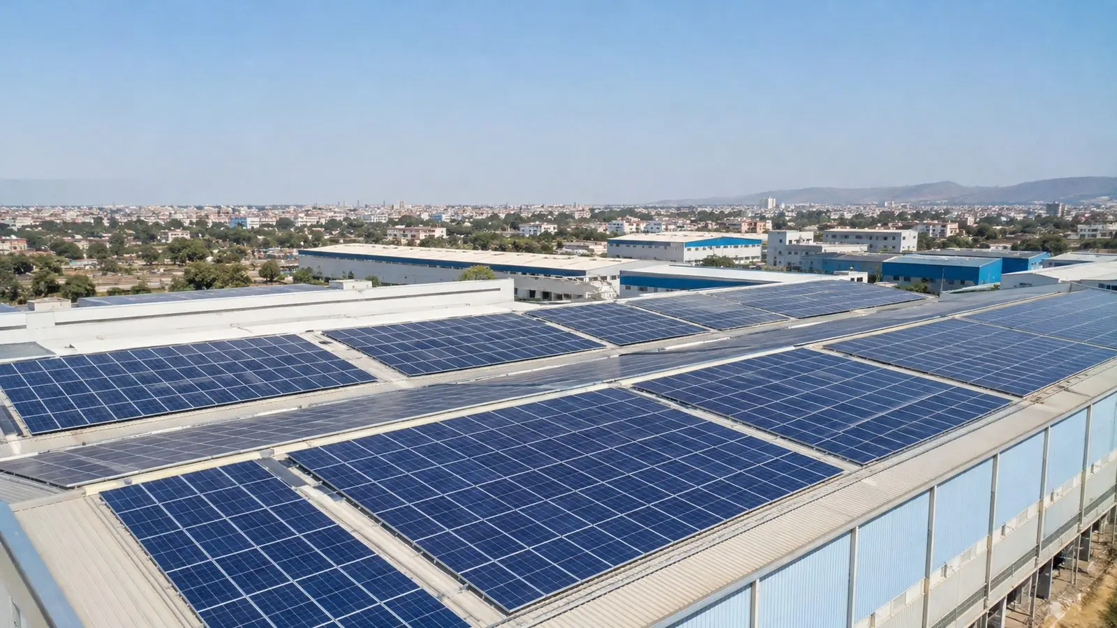 Large commercial rooftop solar installation on a warehouse in a Jaipur industrial area with the city skyline behind
